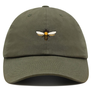 Peut inclure: Une casquette de baseball verte avec un motif d'abeille brodé. L'abeille est jaune et noire avec des ailes blanches.