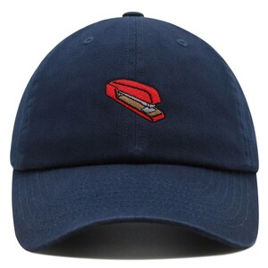 May include: A navy blue baseball cap with an embroidered red stapler on the front.