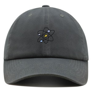 Könnte beinhalten: Eine dunkelgraue Baseballkappe mit einem gestickten Atomdesign. Das Atom ist schwarz mit einem gelben Zentrum und blauen und weißen umlaufenden Partikeln.
