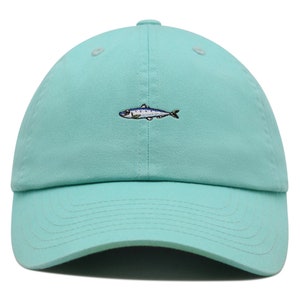 May include: A light teal baseball cap with a small embroidered fish design. The fish is detailed with blue, silver, and black thread. The cap has a curved brim and a fabric strap closure.
