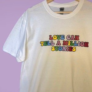 May include: White t-shirt with the text "LOVE CAN TELL A MILLION STORIES" printed in colorful letters.