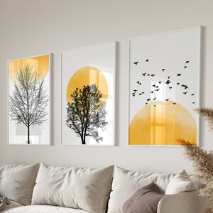 May include: A living room interior with a white sofa, a coffee table, a lamp, and three framed prints on the wall. The prints feature abstract designs with black trees and yellow circles.