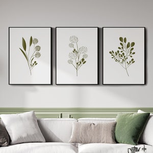 May include: A white sofa with three cushions, a green throw cushion, and a wooden coffee table with a black metal frame. Three framed prints with green botanical illustrations hang on the wall above the sofa.