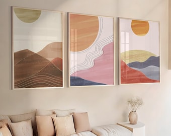 Puede incluir: Tres impresiones artísticas enmarcadas con un diseño de paisaje minimalista. La obra de arte presenta colores cálidos como el naranja, el rosa y el marrón, con un tema de sol y montañas. La habitación también incluye un sofá blanco, una mesa de centro de madera y sillas de ratán.