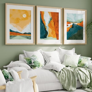 May include: A white sofa with green throw pillows and a green throw blanket. Three framed abstract landscape paintings hang on the wall behind the sofa. A green plant is in the corner of the room.