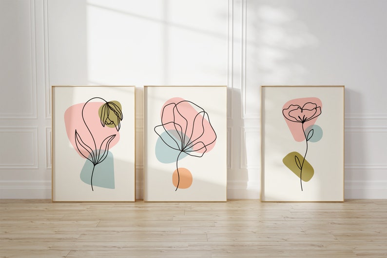 May include: Three framed prints with abstract line drawings of flowers in various colors, including pink, blue, and green. The prints are set against a white wall.
