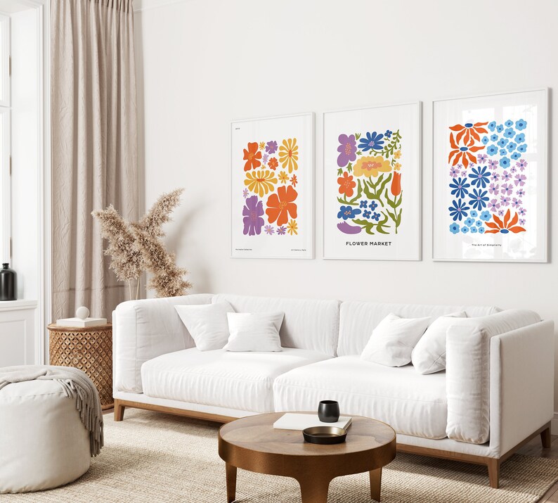 K&ouml;nnte beinhalten: Drei gerahmte Drucke mit bunten Blumenillustrationen. Die Drucke h&auml;ngen an einer wei&szlig;en Wand &uuml;ber einem wei&szlig;en Sofa. Der mittlere Druck hat den Text "FLOWER MARKET" unten.