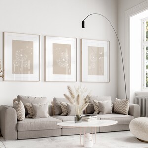May include: A living room interior with a beige sectional sofa, three framed prints of dandelion seeds, a white fluffy armchair, a white coffee table, and a tall black floor lamp.