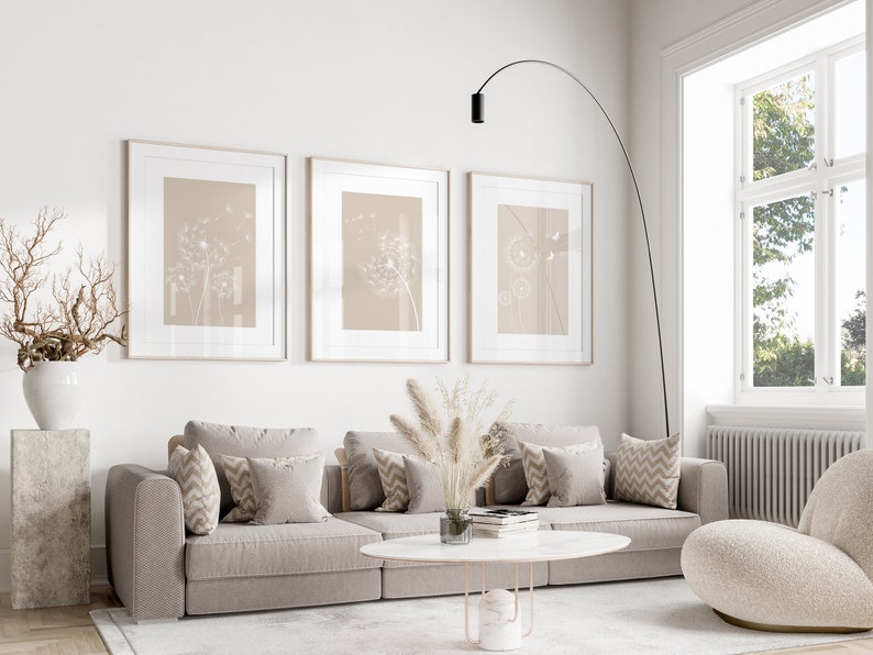 May include: A living room interior with a beige sectional sofa, three framed prints of dandelion seeds, a white fluffy armchair, a white coffee table, and a tall black floor lamp.