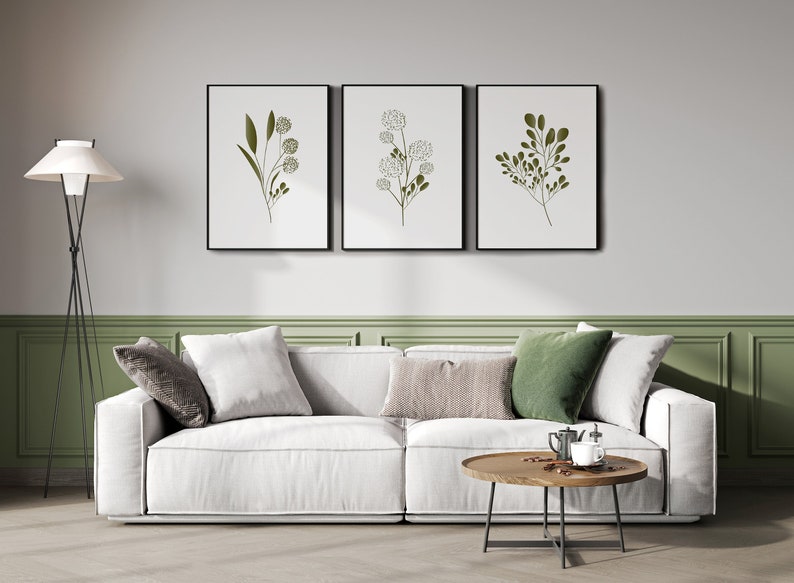 May include: A white sofa with three cushions, a green throw cushion, and a wooden coffee table with a black metal frame. Three framed prints with green botanical illustrations hang on the wall above the sofa.