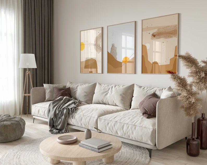 May include: A living room interior with a white sofa, a coffee table, a lamp, and three abstract art prints on the wall. The prints are in shades of brown, beige, and yellow.