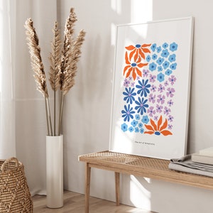 K&ouml;nnte beinhalten: Ein wei&szlig;er gerahmter Druck mit einem farbenfrohen Blumendesign. Der Druck zeigt blaue, orange und lila Blumen auf wei&szlig;em Hintergrund. Der Text "The Art of Simplicity" befindet sich am unteren Rand des Drucks.