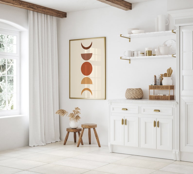 May include: A white kitchen cabinet with two drawers and four doors. The cabinet has gold hardware and a white marble countertop. A framed print with a geometric design of circles and crescent moons in shades of brown and orange hangs on the wall above the cabinet.