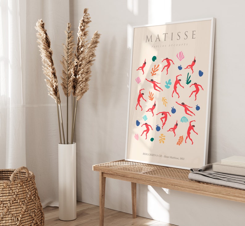 Puede incluir: Una impresi&oacute;n enmarcada de una obra de arte de Matisse titulada "Papiers Decoupes" que presenta figuras rojas bailando sobre un fondo crema con acentos coloridos. La impresi&oacute;n est&aacute; enmarcada en blanco y tiene el nombre del artista y el t&iacute;tulo de la obra de arte impresos en la parte superior.