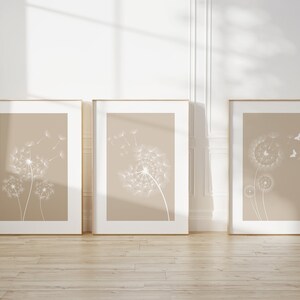 May include: Three framed prints with a beige background and white dandelion illustrations. The dandelions are in various stages of blowing away with seeds.