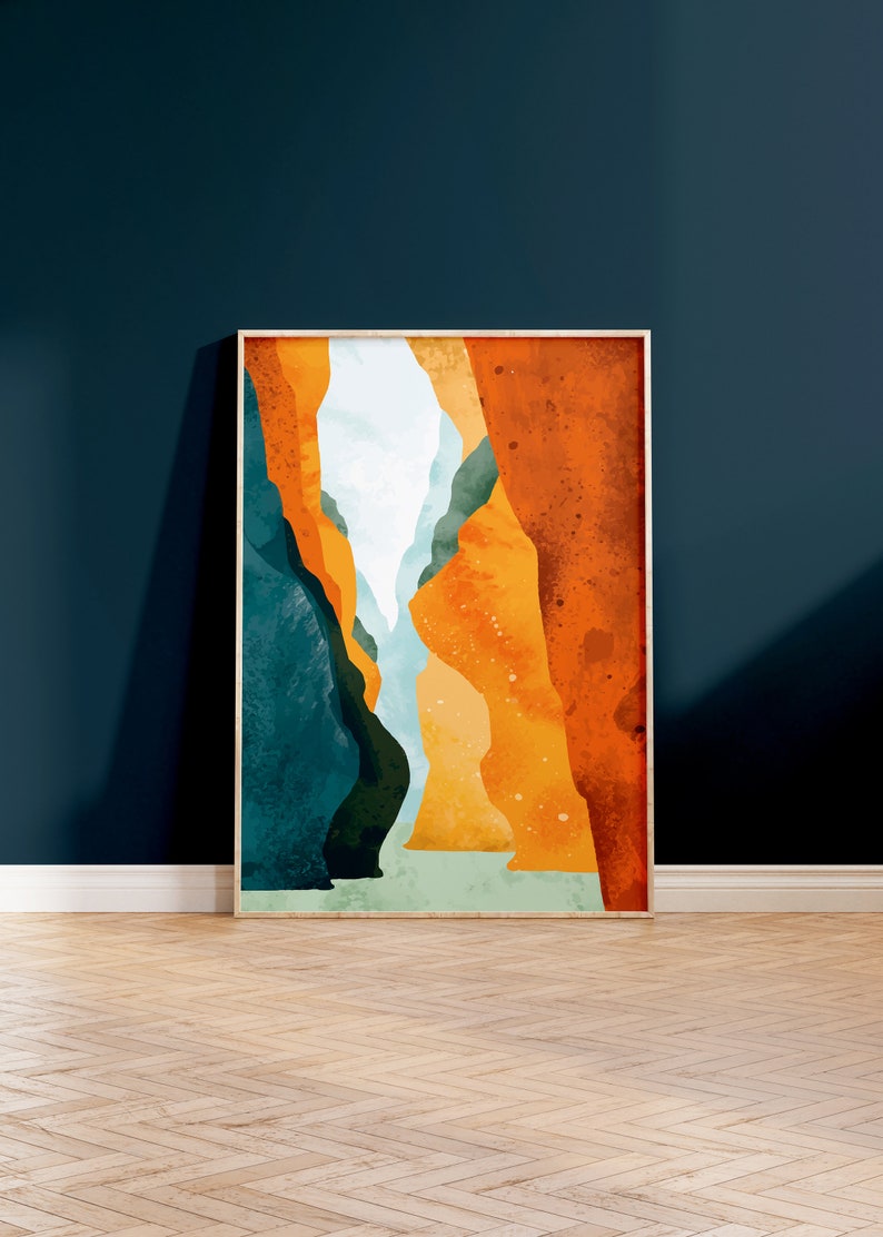 May include: Abstract art print featuring a canyon scene with orange, yellow, blue, and green colors. The print is framed in a light wood frame.
