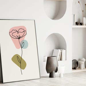 May include: A black framed print with a minimalist line drawing of a flower with pink, green, and blue abstract shapes.