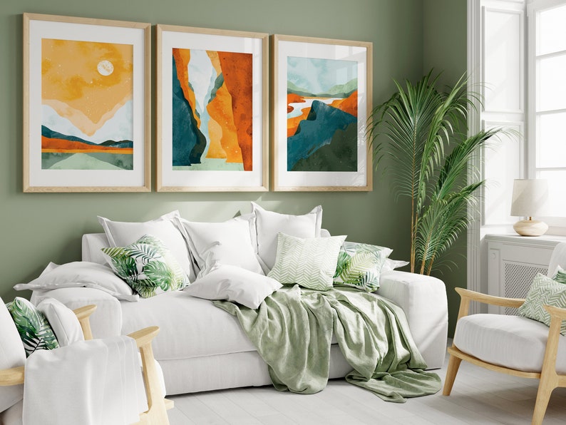 May include: A white sofa with green throw pillows and a green throw blanket. Three framed abstract landscape paintings hang on the wall behind the sofa. A green plant is in the corner of the room.