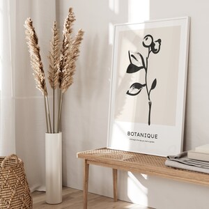 May include: A black and white illustration of a plant with the word "BOTANIQUE" and the text "Life begins the day you start a garden" on a beige background. The illustration is framed in a white frame and is hanging on a wall above a wooden bench.