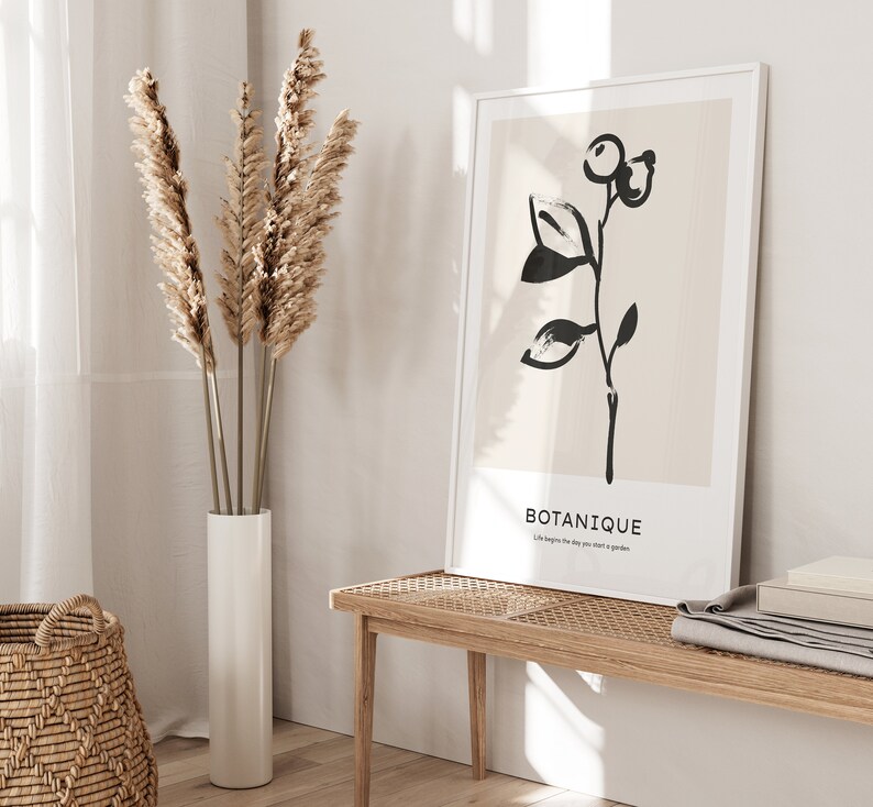 May include: A black and white illustration of a plant with the word "BOTANIQUE" and the text "Life begins the day you start a garden" on a beige background. The illustration is framed in a white frame and is hanging on a wall above a wooden bench.
