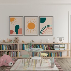 May include: A children's playroom with a light wood bookshelf filled with books. Above the bookshelf are three framed abstract art prints with sun and rainbow designs. A small round table and three stools are in front of the bookshelf.
