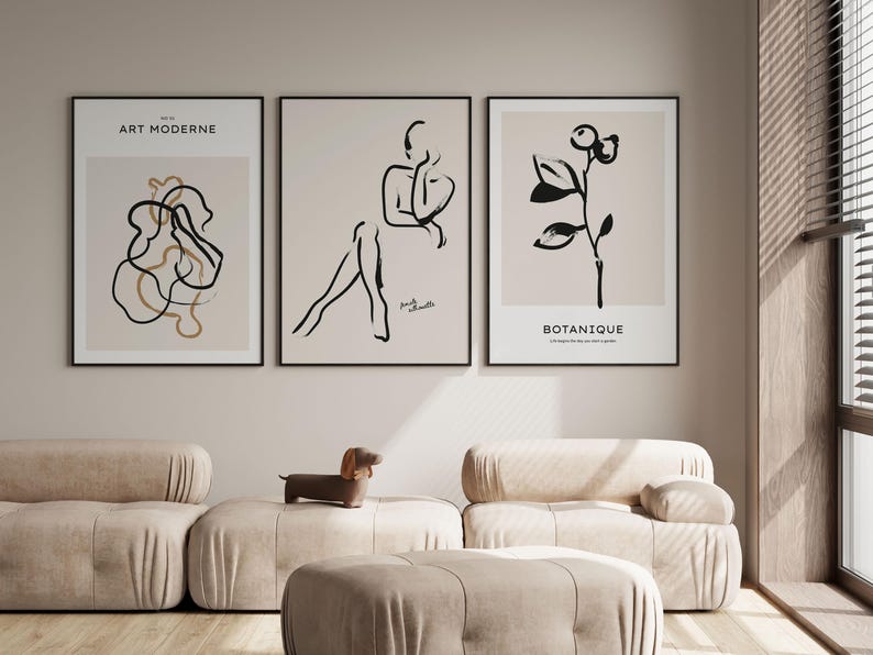 May include: Three black and white line art prints with beige backgrounds. The prints are framed in black and hung on a light beige wall. The prints feature a stylized human figure, a plant, and abstract shapes. The text "ART MODERNE" is on the print with the abstract shapes.
