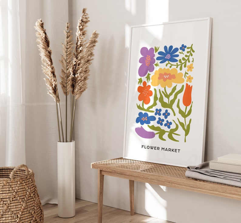 K&ouml;nnte beinhalten: Ein wei&szlig;er gerahmter Druck mit einer bunten Illustration von Blumen und dem Text "FLOWER MARKET". Der Druck h&auml;ngt an einer wei&szlig;en Wand &uuml;ber einer Holzbank.