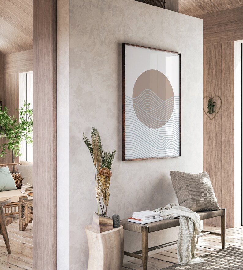 May include: A minimalist wall art print with a brown circle and blue wavy lines on a white background. The print is framed in a dark wood frame and hangs on a light gray wall.