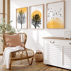 May include: A white cabinet with two drawers and two doors, a wicker chair with a brown cushion, a woven basket, and three framed prints with black silhouettes of trees and yellow circles.