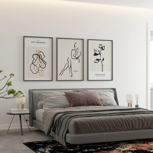 May include: A bedroom with a gray bed, a gray headboard, and three black and white framed prints on the wall. The prints feature abstract line art and the text "Art Moderne" and "Botanique".