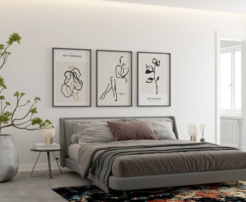 May include: A bedroom with a gray bed, a gray headboard, and three black and white framed prints on the wall. The prints feature abstract line art and the text "Art Moderne" and "Botanique".