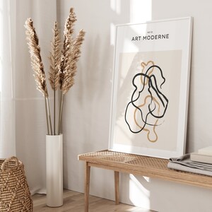 May include: A framed print with the text "ART MODERNE" and a minimalist abstract design featuring black and beige lines on a beige background.