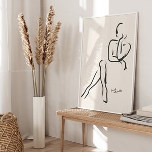 May include: A black and white line drawing of a female silhouette on a beige background. The art print is framed in a white frame and hangs on a white wall. The text "female silhouette" is printed in black at the bottom of the print.