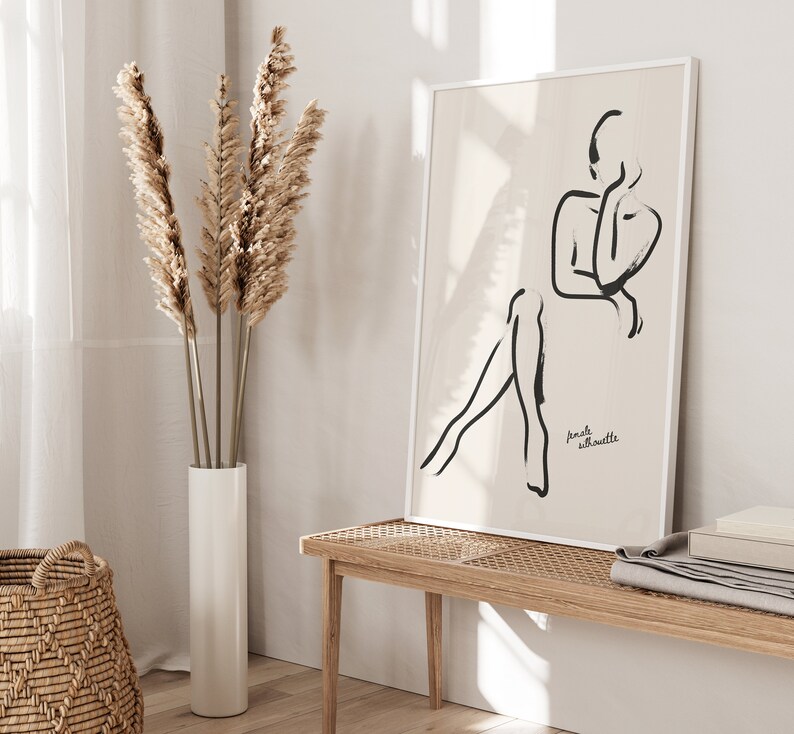 May include: A black and white line drawing of a female silhouette on a beige background. The art print is framed in a white frame and hangs on a white wall. The text "female silhouette" is printed in black at the bottom of the print.