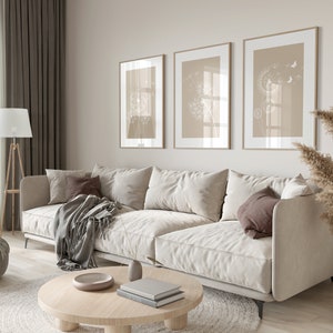 May include: A light beige sectional sofa with a gray throw blanket and brown pillows sits in a living room with a round wooden coffee table and three framed prints of dandelion flowers on the wall.