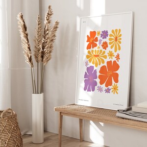 K&ouml;nnte beinhalten: Ein wei&szlig;er gerahmter Druck mit einem farbenfrohen Blumendesign. Der Druck zeigt orange, gelbe und lila Blumen auf wei&szlig;em Hintergrund. Der Text "Art Gallery, Paris" befindet sich am unteren Rand des Drucks.