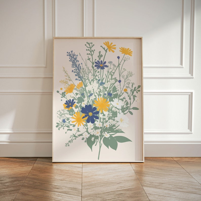 May include: A framed art print featuring a floral bouquet illustration. The artwork showcases yellow, blue, and white flowers with green foliage against a light pink background. The frame is a light wood color, and the print is displayed on a wooden floor.