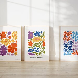 K&ouml;nnte beinhalten: Drei gerahmte Drucke mit bunten Blumenmustern. Die Drucke sind betitelt mit "Morning Dewdrops", "Flower Market" und "The Art of Blooming".