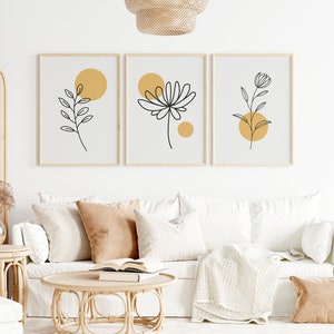 May include: Three minimalist line art prints with black floral designs and yellow circles on a white background. The prints are framed in natural wood and hung on a white wall.