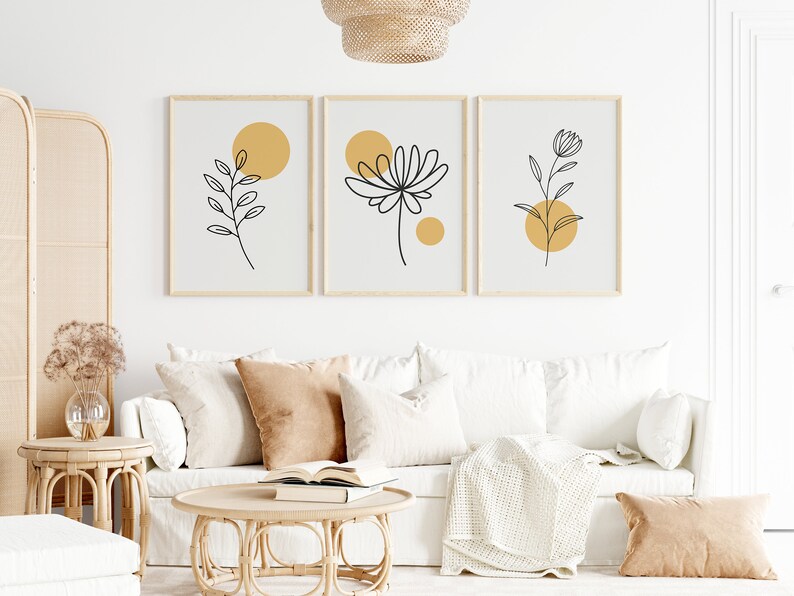 May include: Three minimalist line art prints with black floral designs and yellow circles on a white background. The prints are framed in natural wood and hung on a white wall.