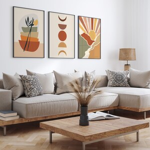 May include: A living room interior with a beige sectional sofa, three framed abstract art prints, a wooden coffee table, and a woven lampshade on a wooden table lamp.