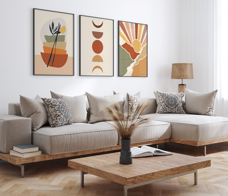 May include: A living room interior with a beige sectional sofa, three framed abstract art prints, a wooden coffee table, and a woven lampshade on a wooden table lamp.