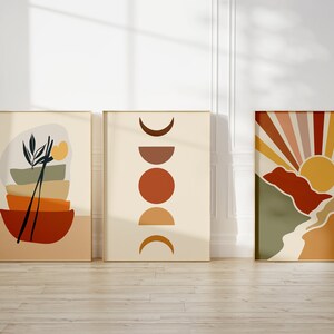 May include: Three abstract art prints in a minimalist style with a neutral background and geometric shapes in shades of orange, yellow, brown, and green. The prints are framed in a light wood frame.