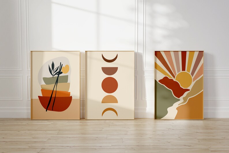 May include: Three abstract art prints in a minimalist style with a neutral background and geometric shapes in shades of orange, yellow, brown, and green. The prints are framed in a light wood frame.