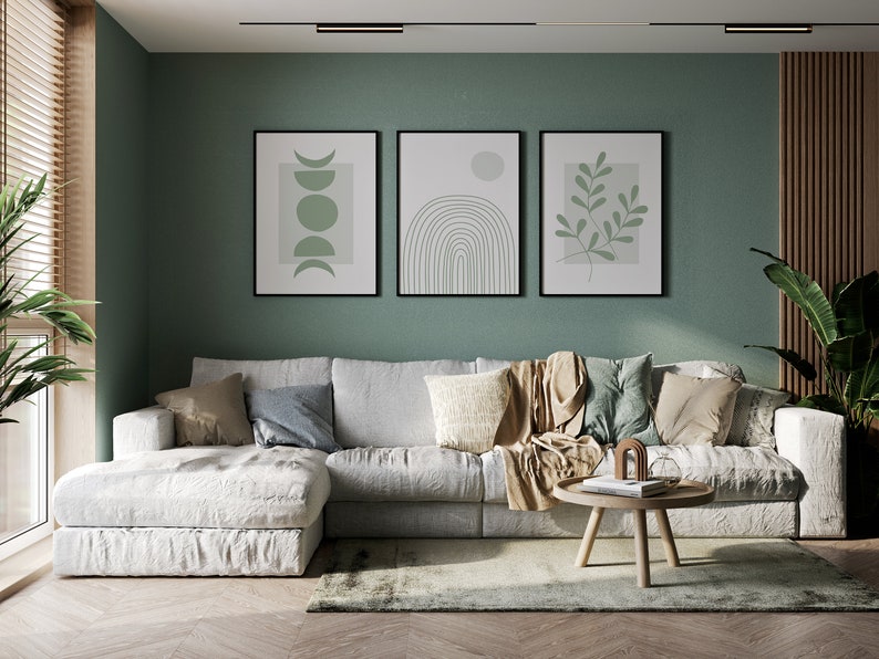 Pu&ograve; includere: Un divano angolare bianco con una coperta di lana marrone e cuscini in un soggiorno con una parete verde e tre stampe incorniciate di arte astratta. La stanza ha un pavimento in legno e un piccolo tavolino da caff&egrave; in legno.
