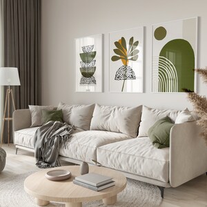 May include: A white sofa with green pillows and a throw blanket sits in a living room with a coffee table and three abstract art prints on the wall. The prints feature green, yellow, and white geometric shapes.