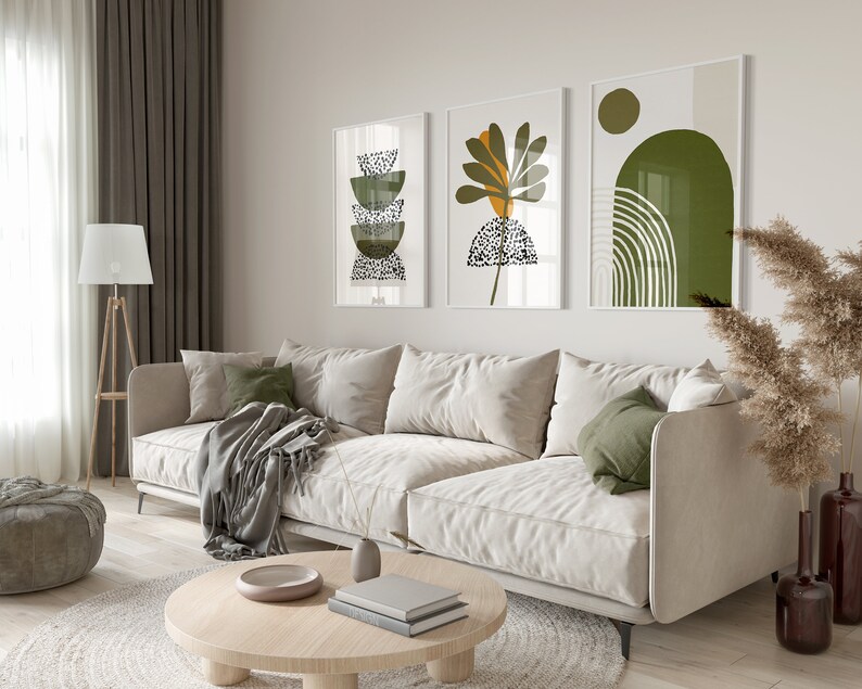 May include: A white sofa with green pillows and a throw blanket sits in a living room with a coffee table and three abstract art prints on the wall. The prints feature green, yellow, and white geometric shapes.
