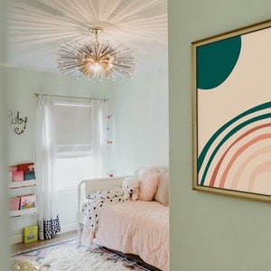 May include: A framed abstract art print with a gold frame hangs on a mint green wall. The artwork features a teal circle and a rainbow design in shades of pink, teal, and beige. The room has a bed with pink bedding.