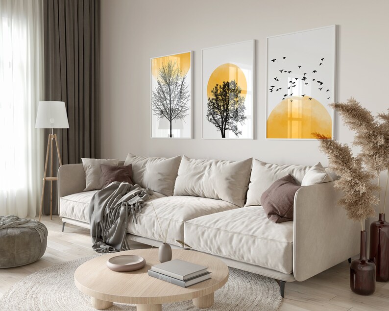 May include: A living room interior with a white sofa, a coffee table, a lamp, and three framed prints on the wall. The prints feature abstract designs with black trees and yellow circles.