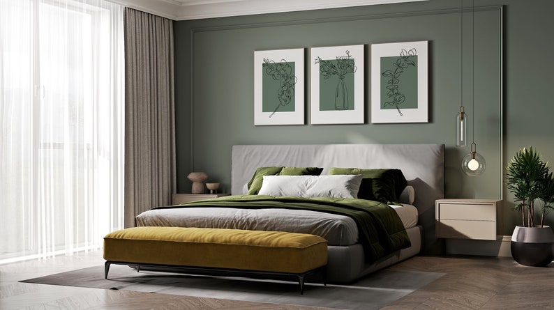 May include: A bedroom with a grey bed, green bedding, and a yellow bench at the foot of the bed. There are three framed prints on the wall behind the bed, each with a line drawing of a plant. A small bedside table with two drawers is on the right side of the bed.